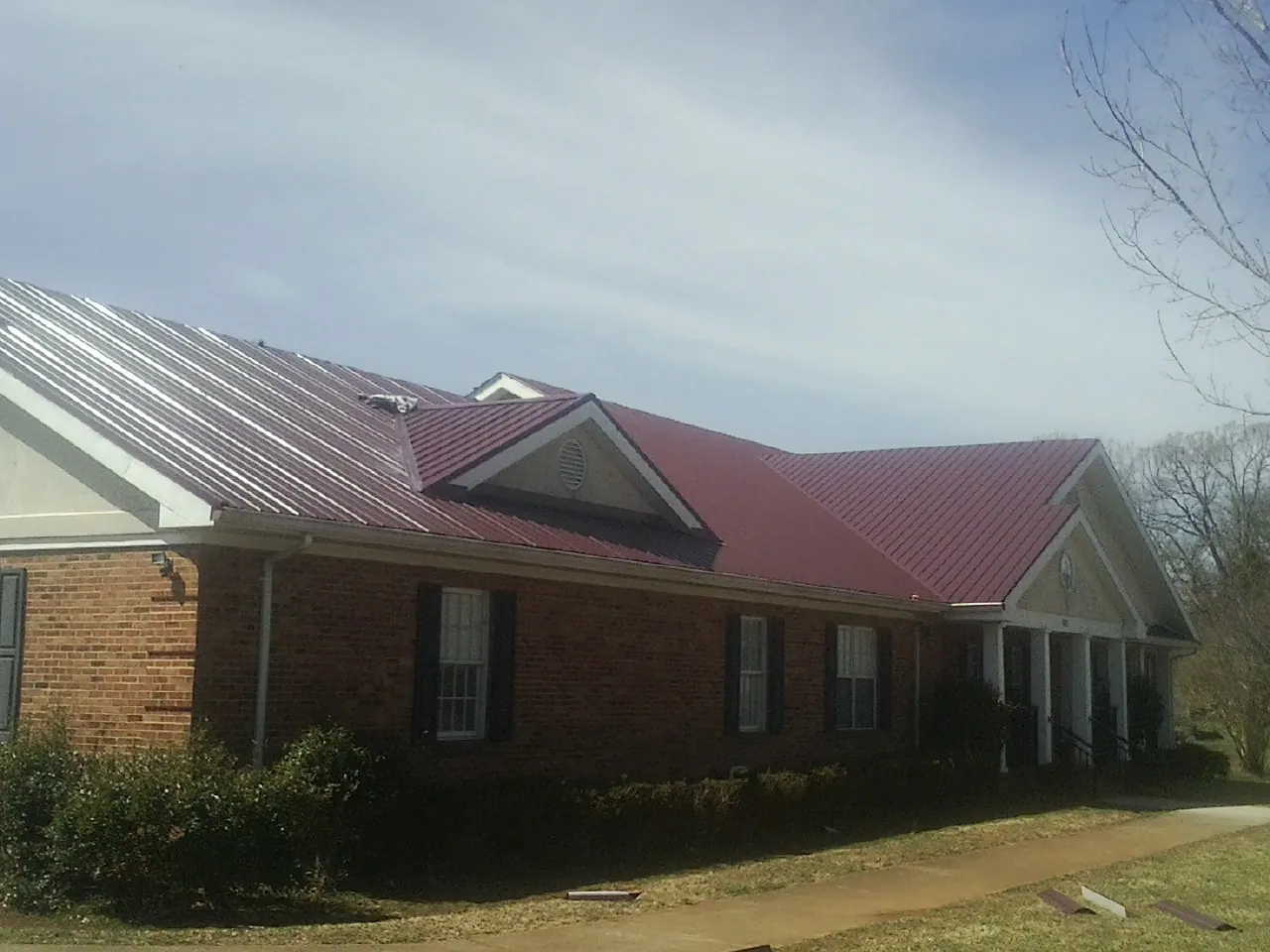Red metal roof with gabled entries on a long brick building, from a Hail Damage Roof Repair job in Howard