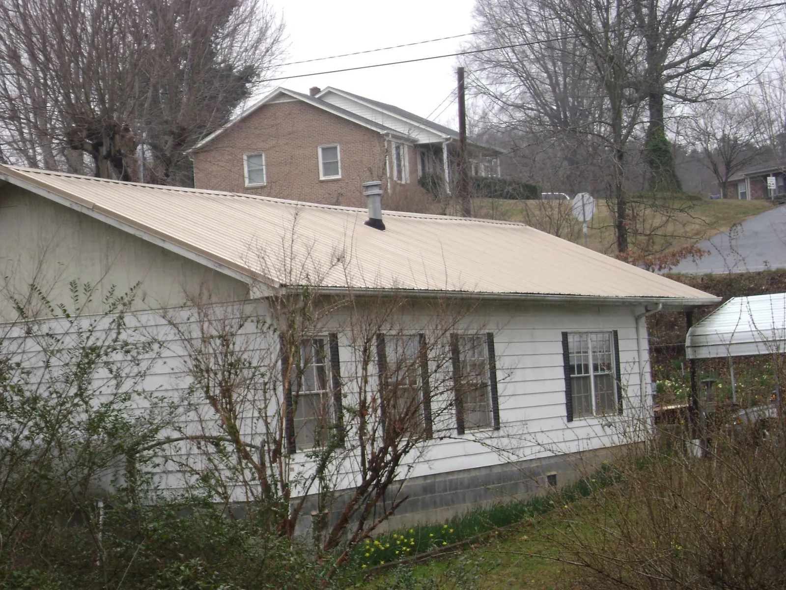 Tan metal roof on a white sided house set into a hillside — Commercial Roofing by Roofing Brothers in Howard