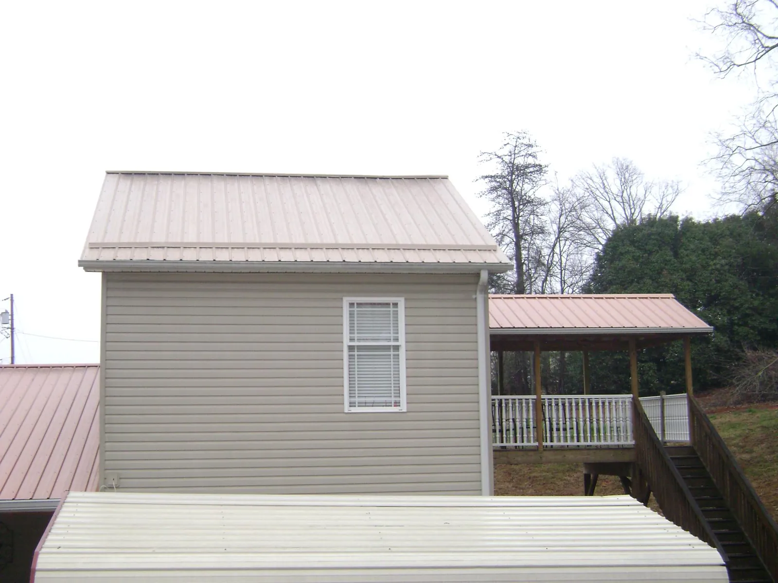 Tan metal roofs on a two story addition and attached porch, from a Roof Replacement job in Howard